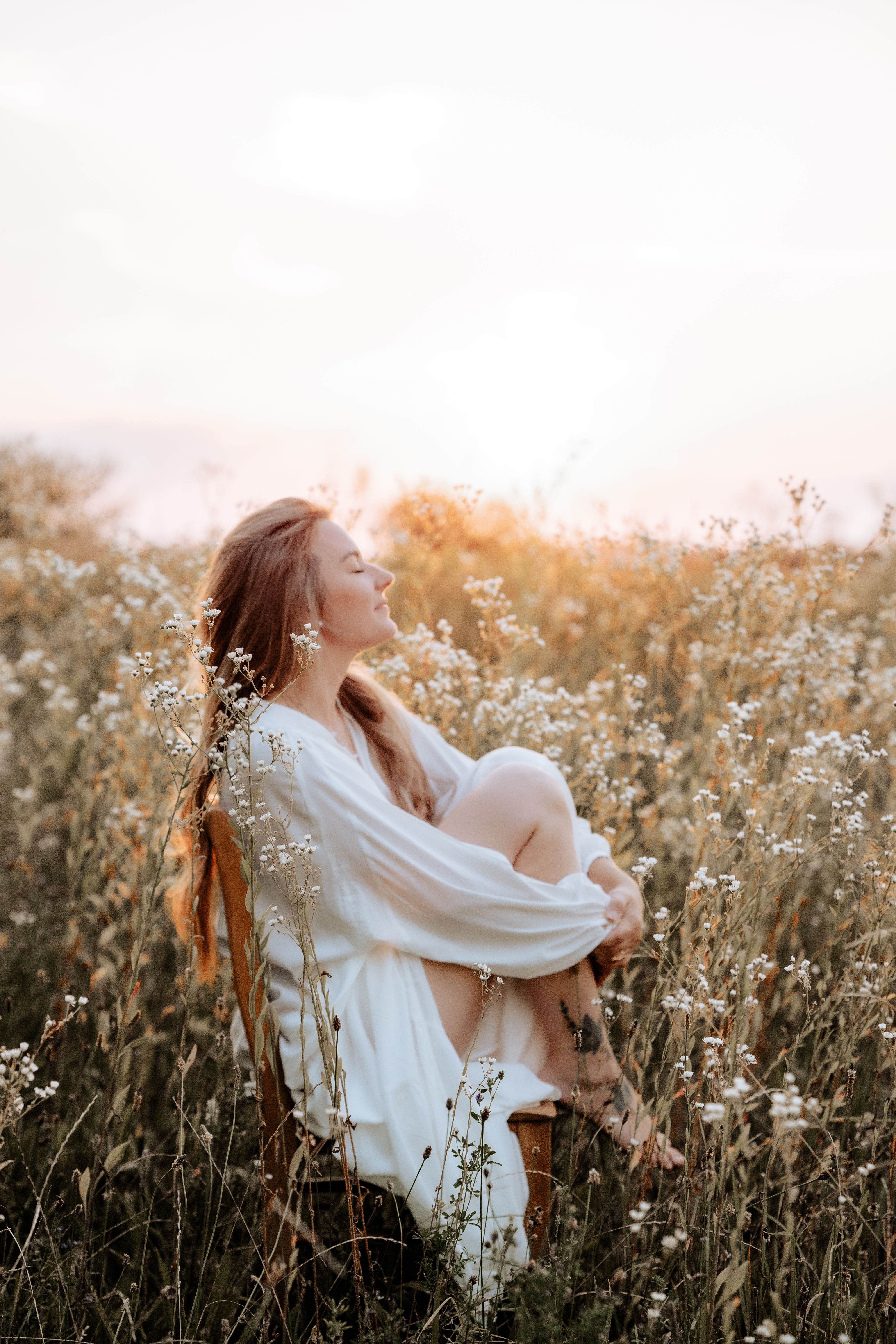 Stephanie sitzt bei Sonnenuntergang auf einem Holzstuhl in einer Blumenwiese